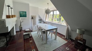 A dining area with a table and chairs, a vase with flowers, and a window with a view of greenery.