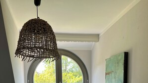 A room with a large arched window, a white cabinet with drawers, a hanging woven light fixture, and a vase with green plants on the window sill.
