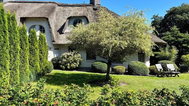 A house with a thatched roof, surrounded by a well-maintained garden with various plants and a lawn.