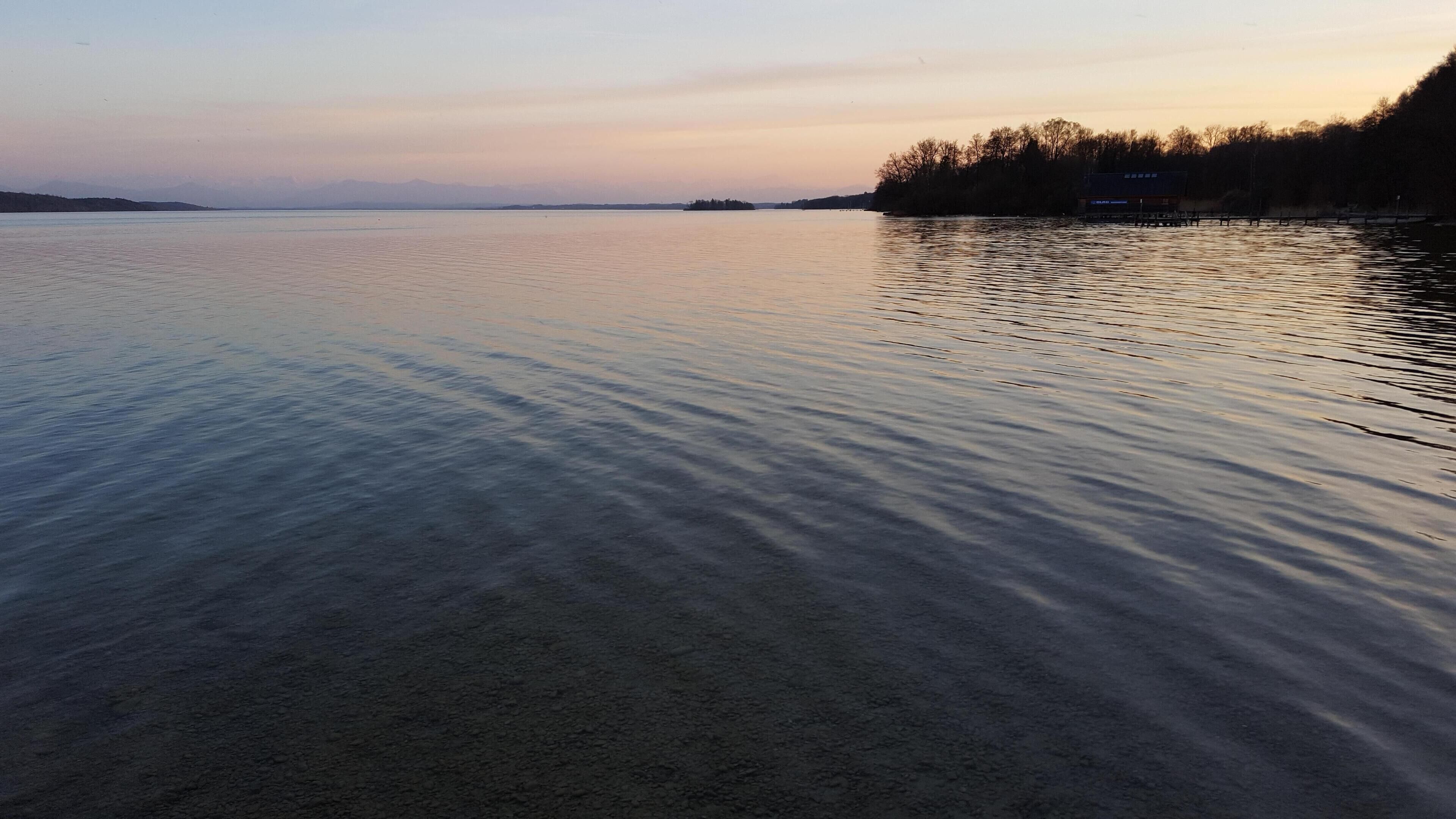 A calm lake with a distant shoreline and trees.