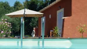 A swimming pool with a clear water surface, a beige umbrella, and a statue in the background. - Sun holidays in the calm of the French Riviera. 3 *** apartment (Les Adrets-De-L'estérel)
