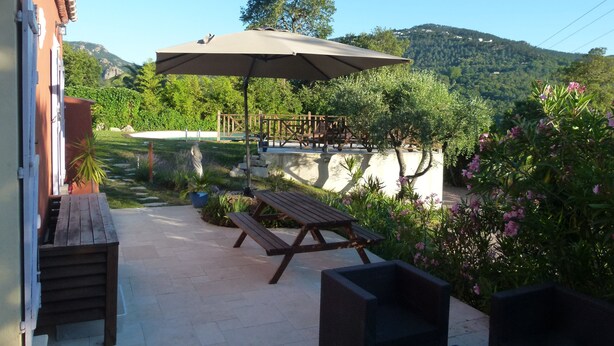 A patio with a wooden bench and a large umbrella, surrounded by greenery and a view of hills. - Sun holidays in the calm of the French Riviera. 3 *** apartment (Les Adrets-De-L'estérel)