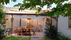 A cozy outdoor patio with a wooden table and chairs, surrounded by lush greenery and a white lace canopy. - Apartment Le Solutré (Chardonnay)