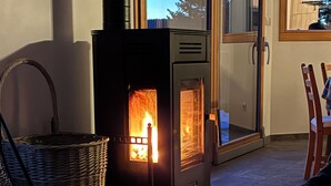 Une pièce chaleureuse avec une cheminée, des meubles en osier et une vue à travers une porte vitrée.
