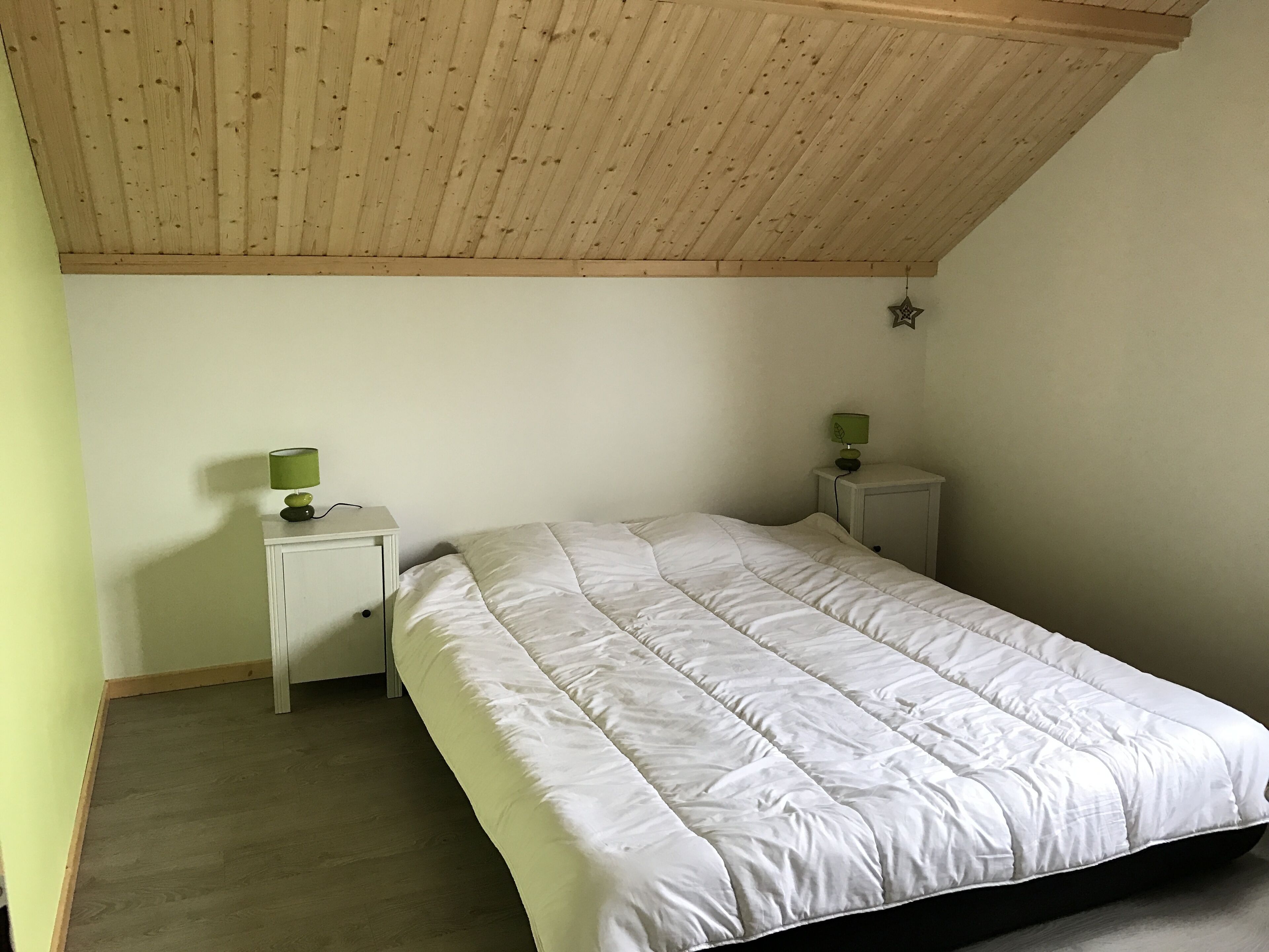 A bedroom with a wooden ceiling, a white bed, and two bedside tables with lamps.