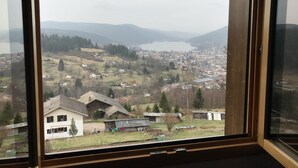 Une vue depuis une fenêtre donnant sur une ville, avec un lac, des maisons et des collines à l’horizon.