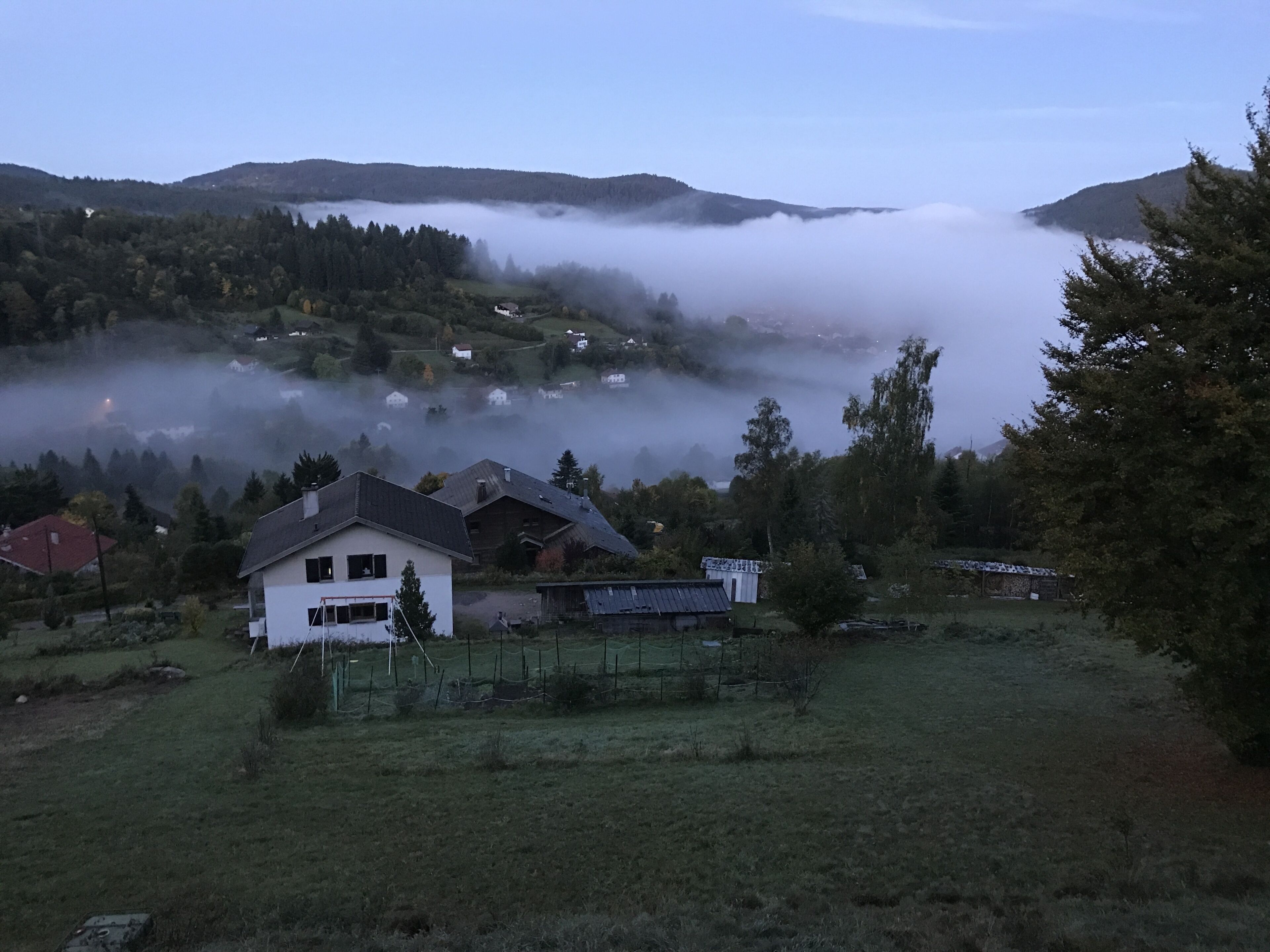 A rural landscape with houses, a fence, and a mist-covered valley.