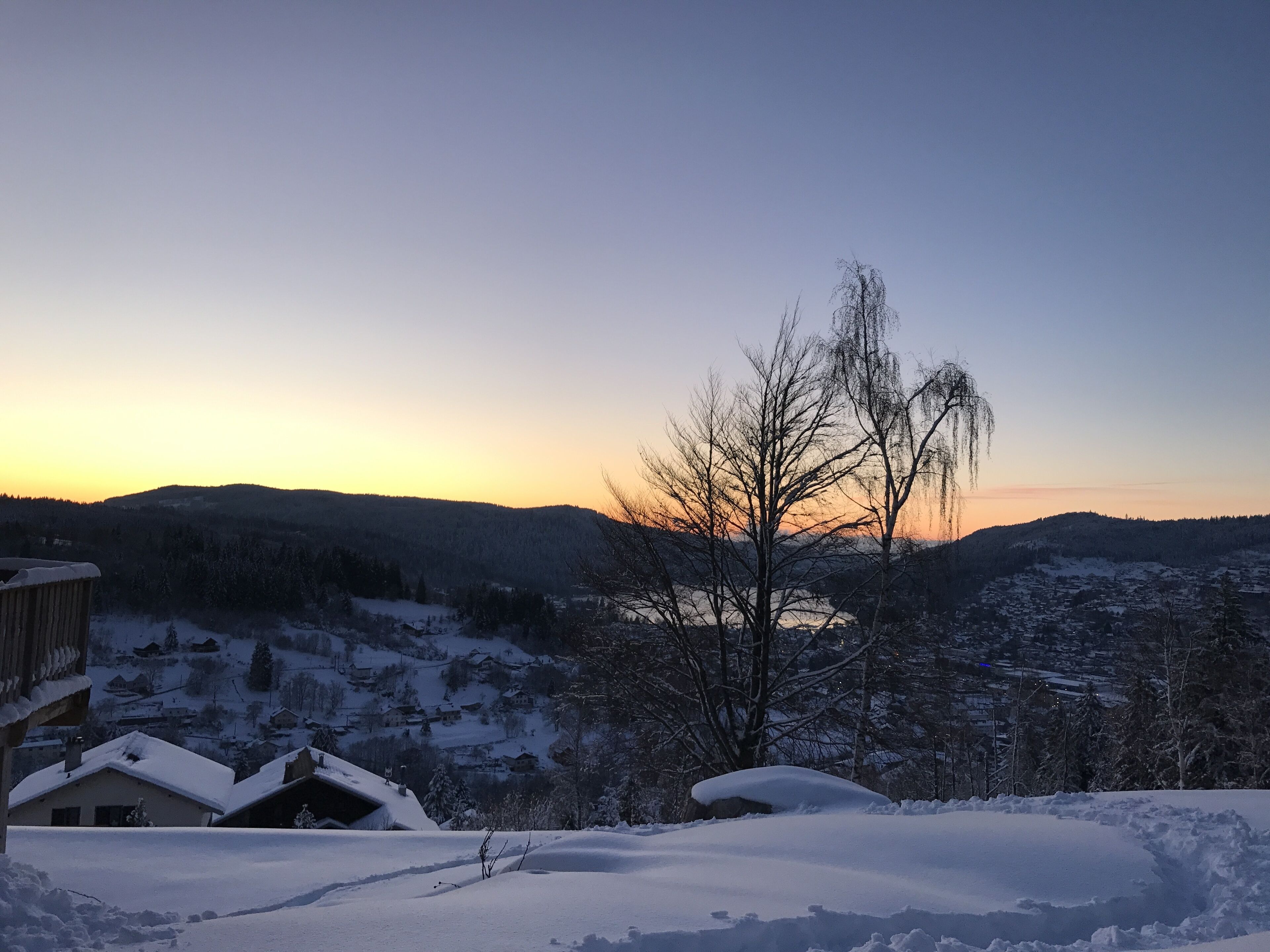 A snowy landscape with a clear sky at dusk, featuring a house with a snow-covered roof and a view of the surrounding hills.