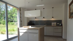 Una cocina moderna con una isla grande, iluminación colgante y vistas a zonas verdes.