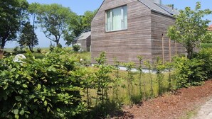 Una casa moderna de madera con un ventanal grande, rodeada de exuberante vegetación y árboles.