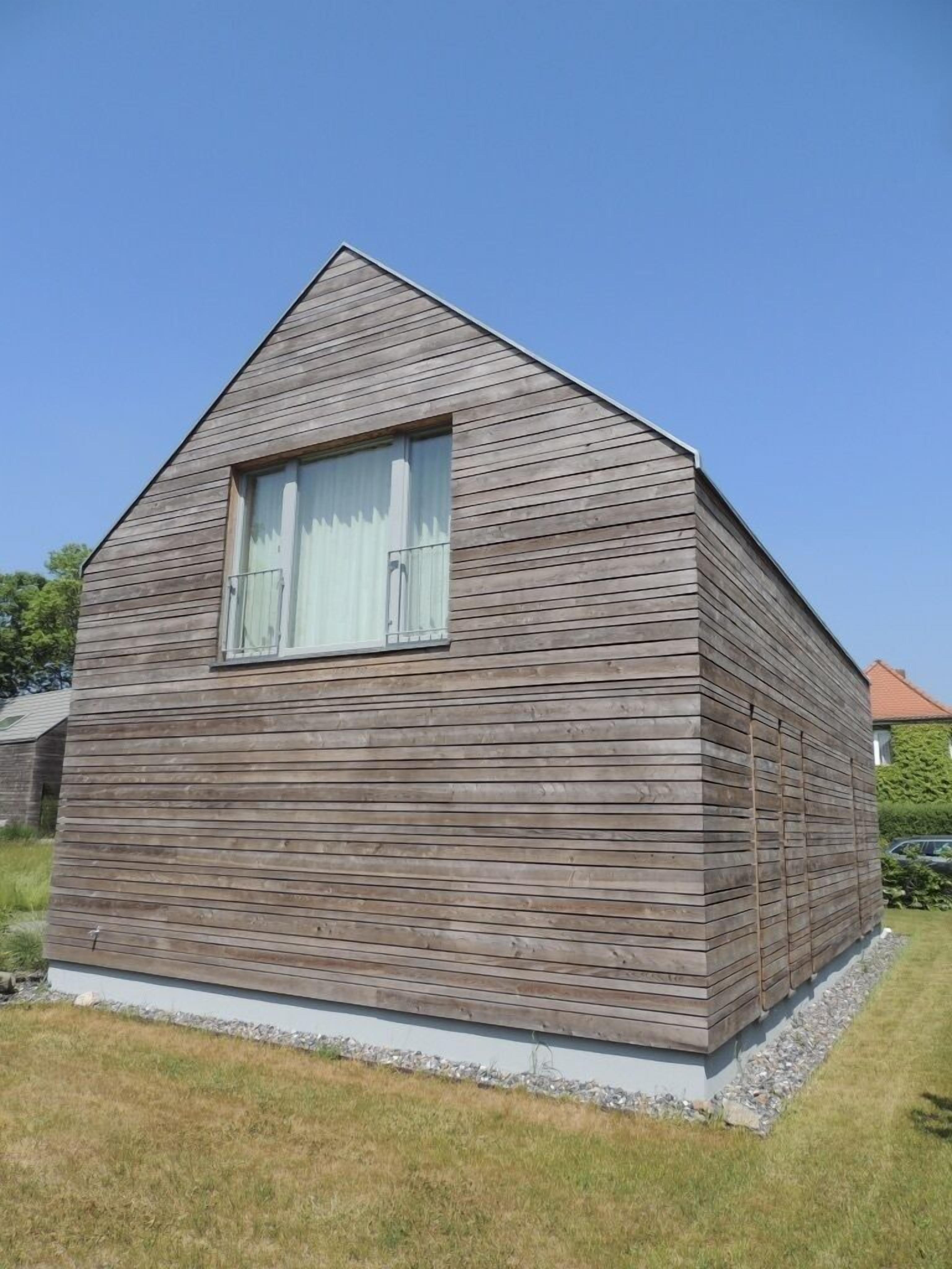 Une maison en bois d’un seul étage, avec un toit à pignon et une grande fenêtre.