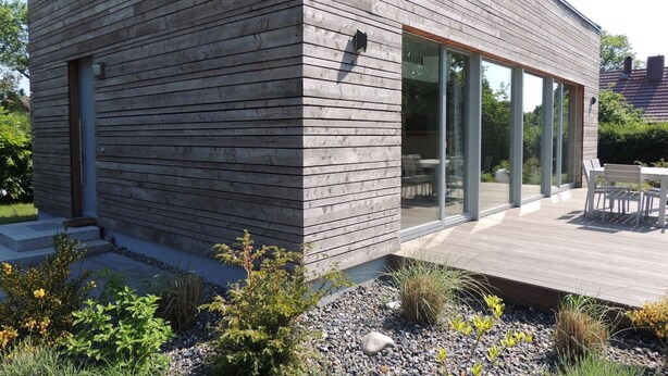 Una casa moderna con fachada de madera, amplios ventanales y una terraza con mobiliario exterior.