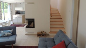 Una sala de estar moderna con chimenea, una escalera y una cocina al fondo.