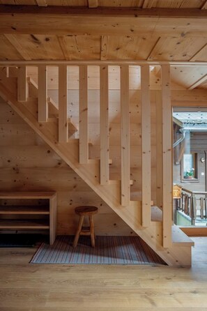A wooden staircase with a handrail, a small stool, and a view of an outdoor area with a railing.