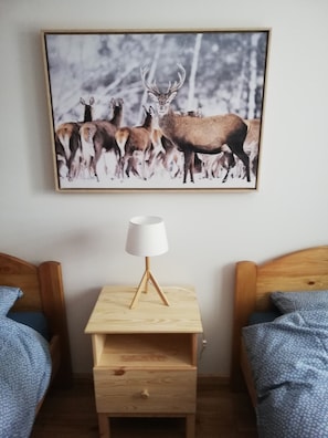 Um quarto com duas camas de madeira, uma mesinha de cabeceira com abajur e um quadro com pintura de animais selvagens na parede.