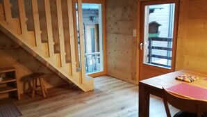 Interior de madera con una escalera, una mesa con cojín y una puerta que da al exterior.