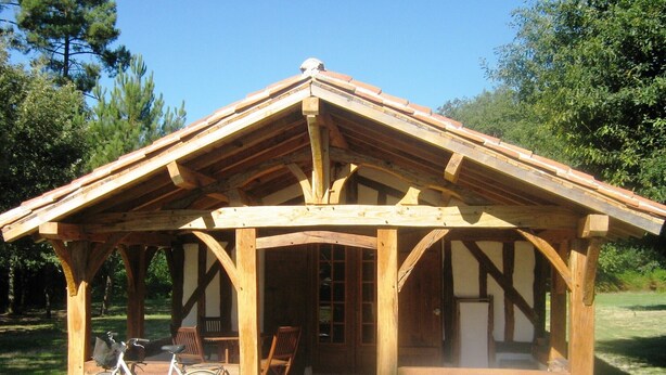 A wooden pavilion with a pitched roof, built-in benches, and a bicycle parked outside. - In the heart of the Landes forest, traditional half-timbered gîte, 4pers. (Argelouse)