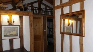 A room with exposed wooden beams, a wooden door, a framed picture, a mirror, and a small table. - In the heart of the Landes forest, traditional half-timbered gîte, 4pers. (Argelouse)