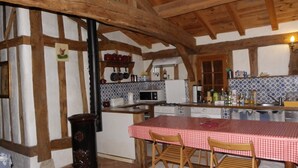 A rustic kitchen with exposed wooden beams, a checkered tablecloth-covered table, and a tiled backsplash. - In the heart of the Landes forest, traditional half-timbered gîte, 4pers. (Argelouse)