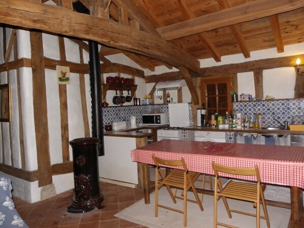 A rustic kitchen with exposed wooden beams, a checkered tablecloth-covered table, and a tiled backsplash. - In the heart of the Landes forest, traditional half-timbered gîte, 4pers. (Argelouse)