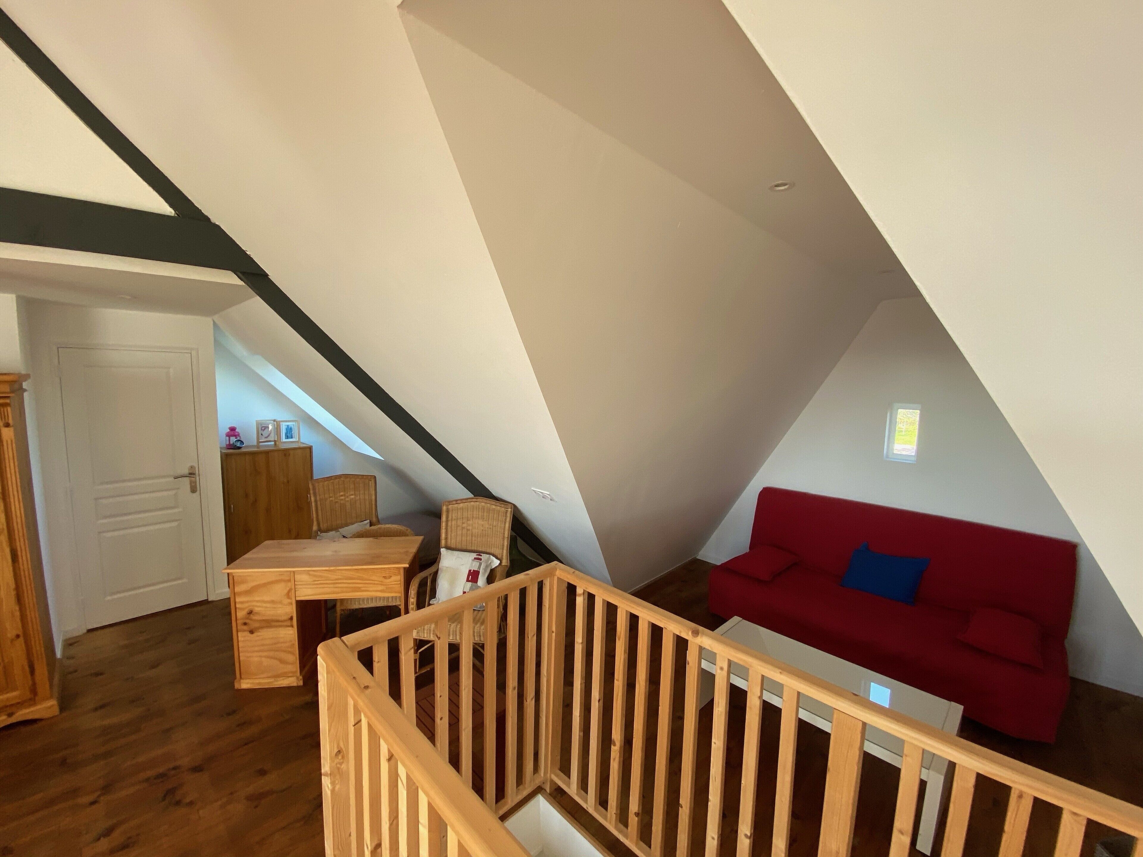 Une pièce de style loft avec un escalier en bois, un canapé rouge et un coin repas comprenant une table et des chaises en bois.