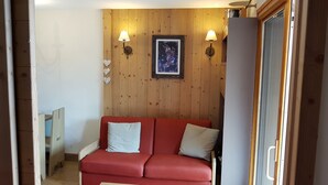 Una habitación acogedora con una pared de madera, un sofá rojo, dos lámparas de pared y un cuadro enmarcado.
