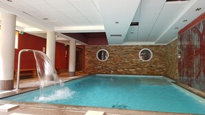 Una piscina interior con cascada, paredes de piedra y una pared decorada en rojo.