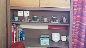 Un mueble de madera con estantes que contienen libros, tazas y una botella roja.