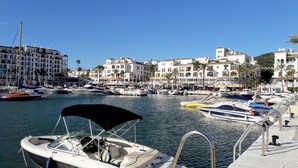 A marina with boats docked, surrounded by buildings with balconies and palm trees. - Estepona, Casares apartment breathtaking sea and golf views (Casares)