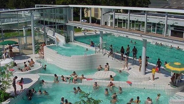 Ein großes Schwimmbecken im Freien mit mehreren Bereichen und einem durch Glas abgeschlossenen Bereich.