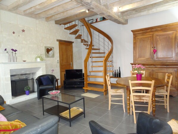 Una sala de estar con chimenea, televisor, escalera de madera y comedor.
