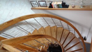 Eine hölzerne Wendeltreppe mit Metallgeländer und einem Regal darüber mit Büchern und Dekorationsobjekten.