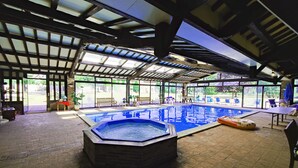 An indoor swimming pool with a hexagonal hot tub, surrounded by lounge chairs and a covered patio area. - CHARMING RESIDENCE with swimming pool and indoor spa (Conches-en-Ouche)