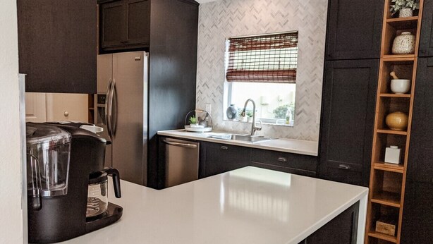 A modern kitchen with dark cabinetry, a white countertop, a built-in coffee maker, and a window with a view. - Put some MAGIC into your vacation.  Disney only 20 minutes away! (Haines City)