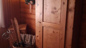 Un intérieur en bois avec un meuble en bois, un panier en osier contenant des skis et un luminaire fixé au mur.
