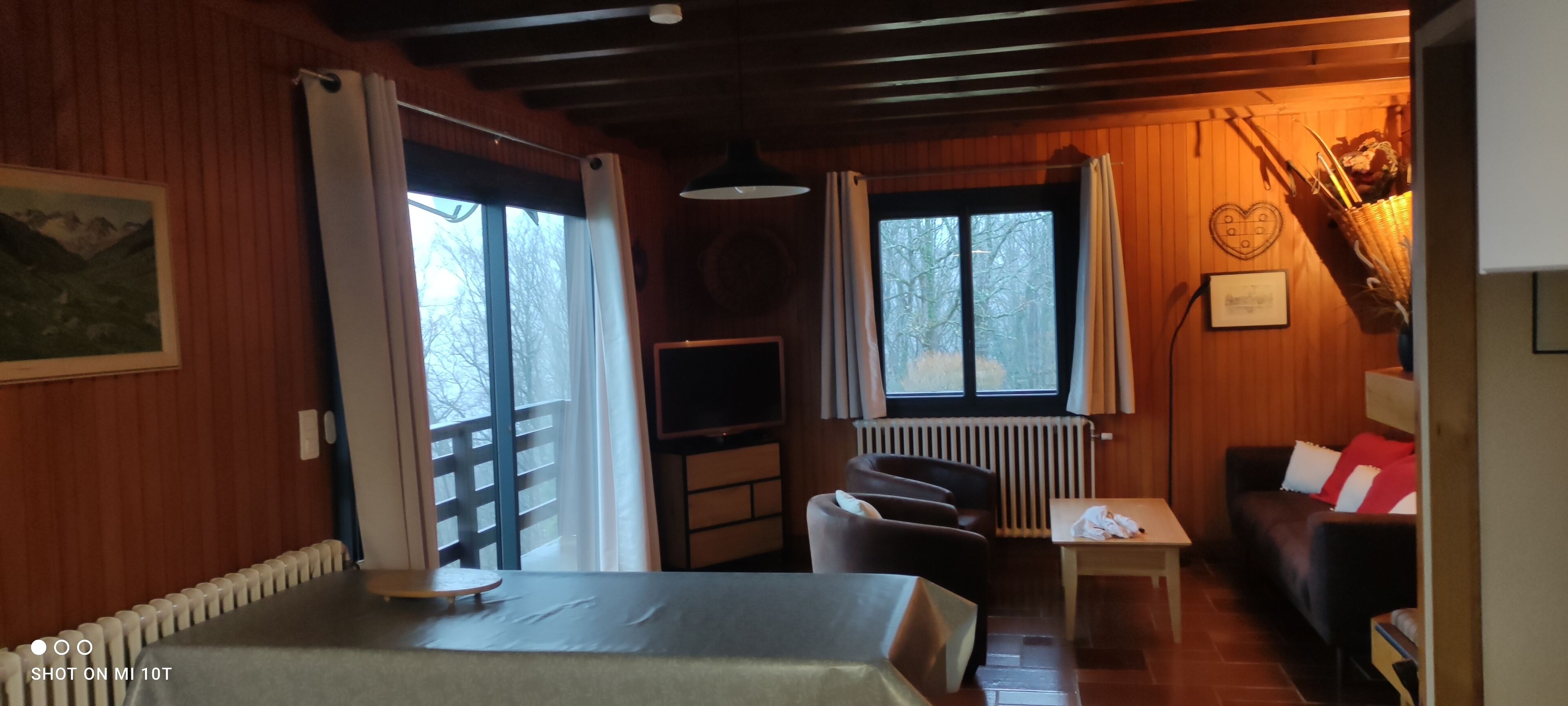 Ein gemütliches Zimmer mit Holzvertäfelung, einem Esstisch, einer Couch und einem Fernseher.