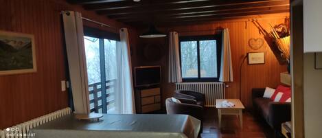 Ein gemütliches Zimmer mit Holzvertäfelung, einem Esstisch, einer Couch und einem Fernseher.