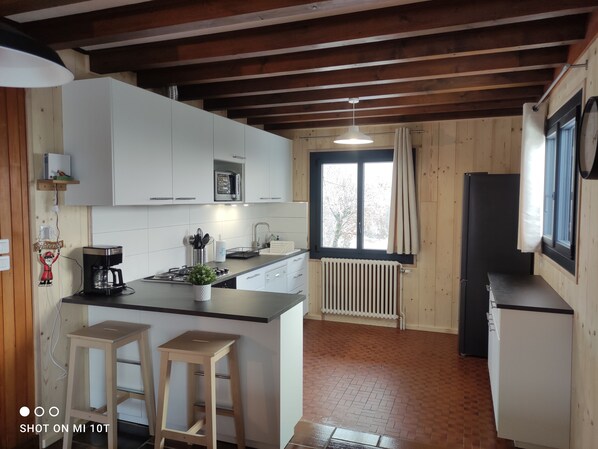 A kitchen with white cabinets, a coffee maker, a sink, and a window with curtains. - NOVELTY. Exceptional view, Hérisson waterfalls (Bonlieu)