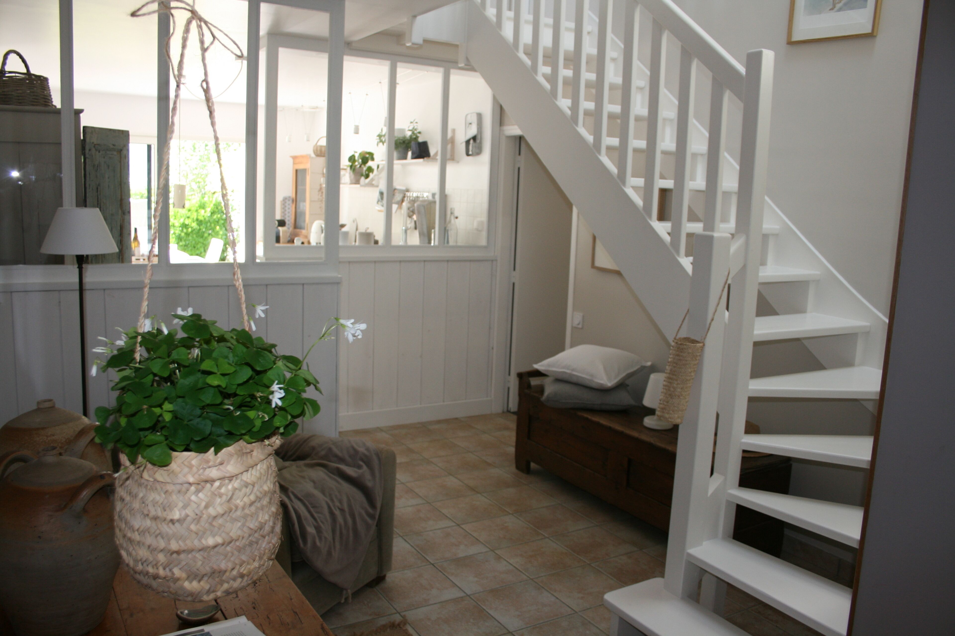 A cozy room with a wooden table, a woven basket with a plant, a lamp, and a staircase leading to another room.
