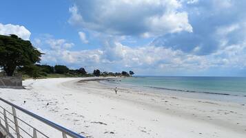 A beach with a stone wall, a metal railing, and a person walking.
