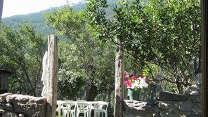 An outdoor seating area with stone walls and white plastic chairs, overlooking a mountainous landscape. - Serre Chevalier Apartment in a house Country, nice amenities. (Saint-Chaffrey)