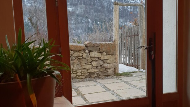A wooden door leading to a stone wall and a wooden fence. A potted plant is on a table in the foreground. - Serre Chevalier Apartment in a house Country, nice amenities. (Saint-Chaffrey)