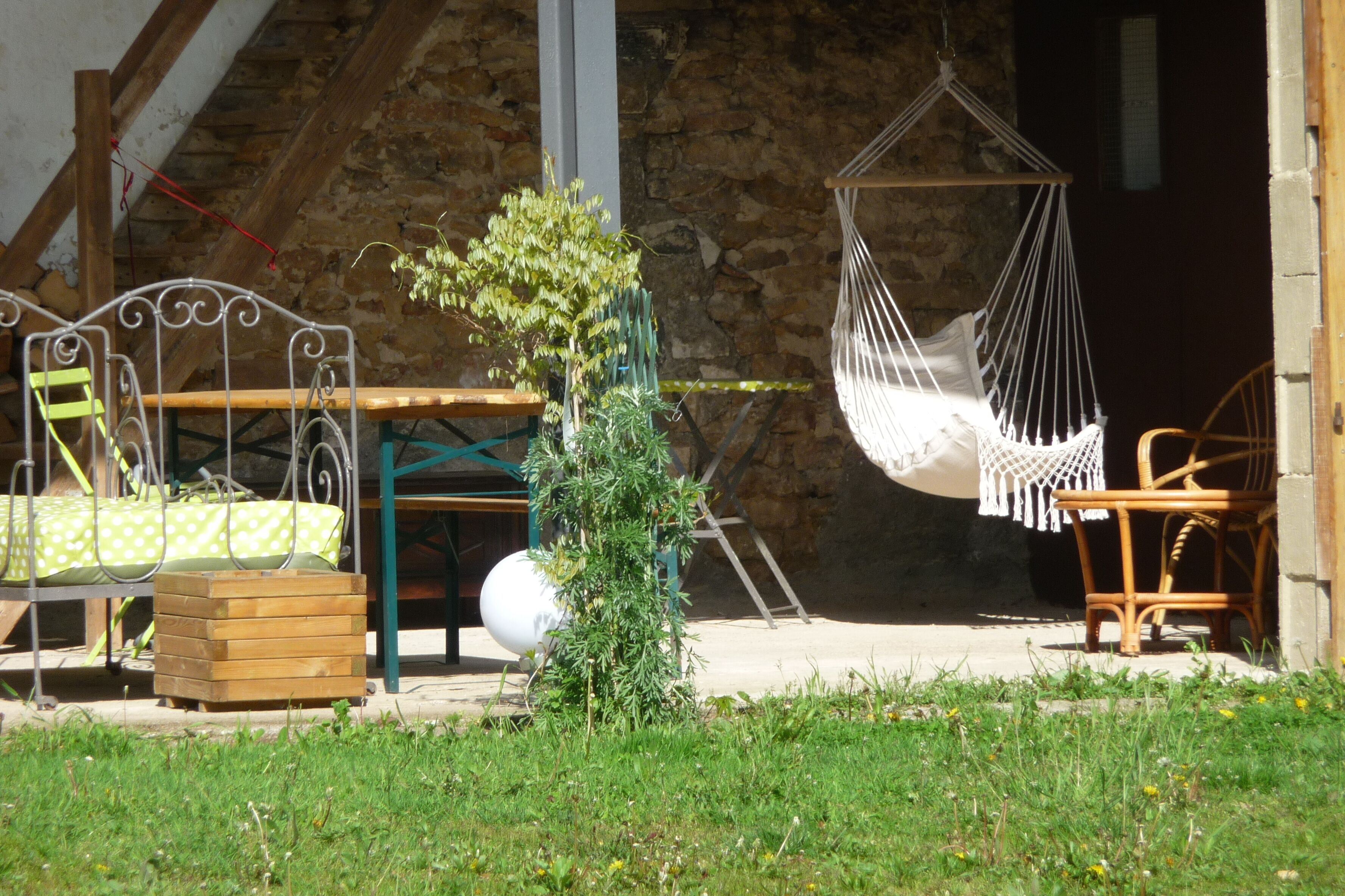 A rustic outdoor seating area with a hammock, a wooden bench, and a metal table.