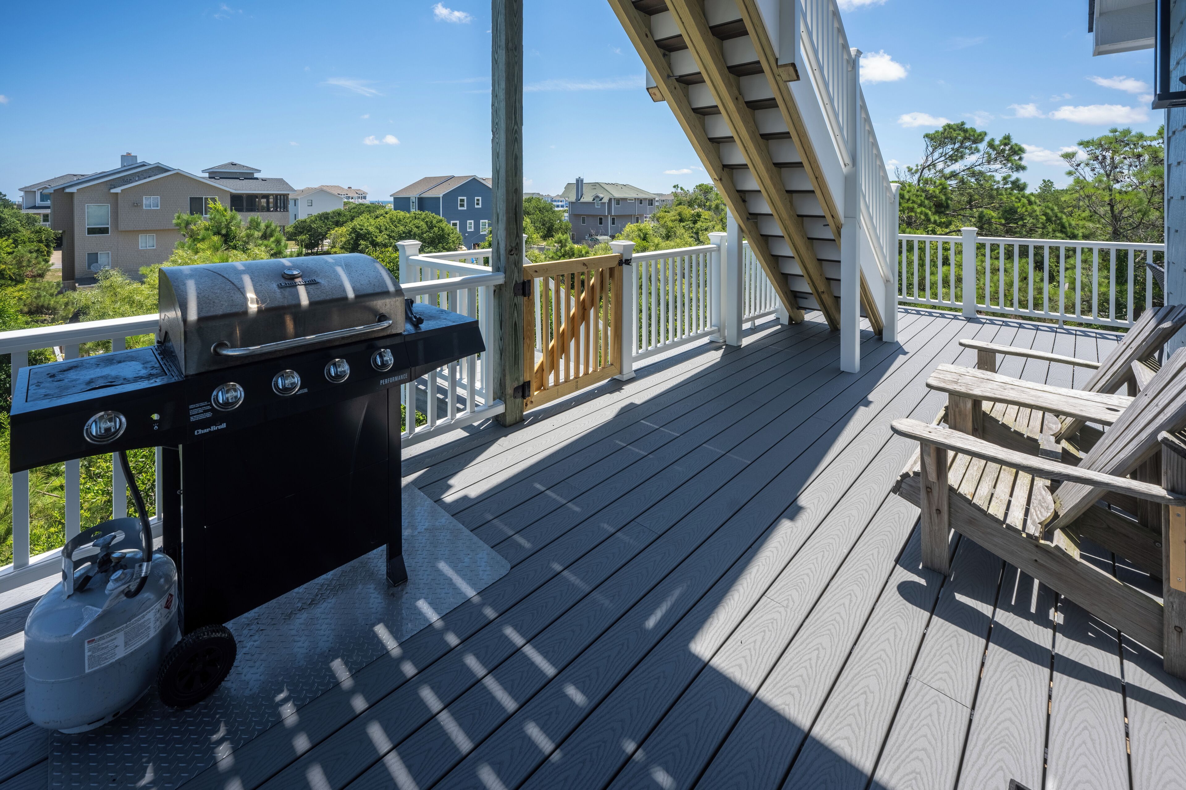 A deck with a grill, a gas tank, and a wooden bench.