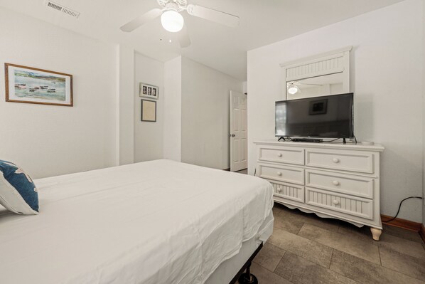 A bedroom with a bed, a dresser, a television, and a ceiling fan. - Crazy4Shore: Dog-friendly, Large Private Pool, Hot Tub, 1500 Ft to Beach Access (Corolla)