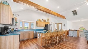 A spacious kitchen with wooden cabinets, a large island with bar stools, and a view of the outdoors. - Crazy4Shore: Dog-friendly, Large Private Pool, Hot Tub, 1500 Ft to Beach Access (Corolla)