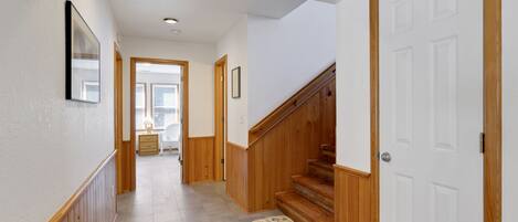 Un couloir aux murs lambrés, une porte blanche et un escalier.