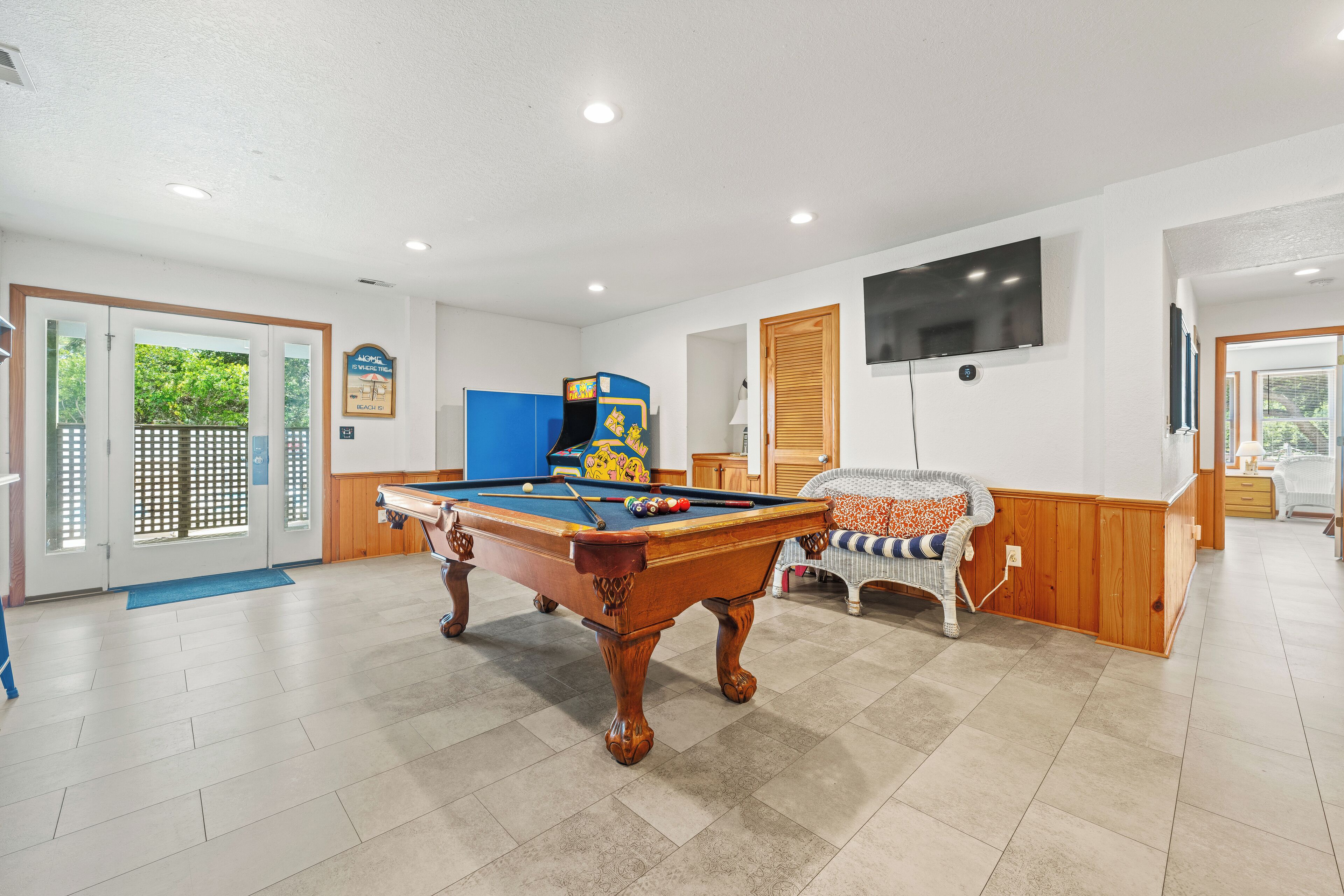 A pool table in a room with a television mounted on the wall, wooden flooring, and a door leading outside.