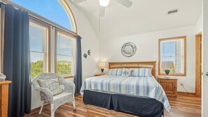 A bedroom with a large bed, a wicker chair, and a ceiling fan. - Crazy4Shore: Dog-friendly, Large Private Pool, Hot Tub, 1500 Ft to Beach Access (Corolla)