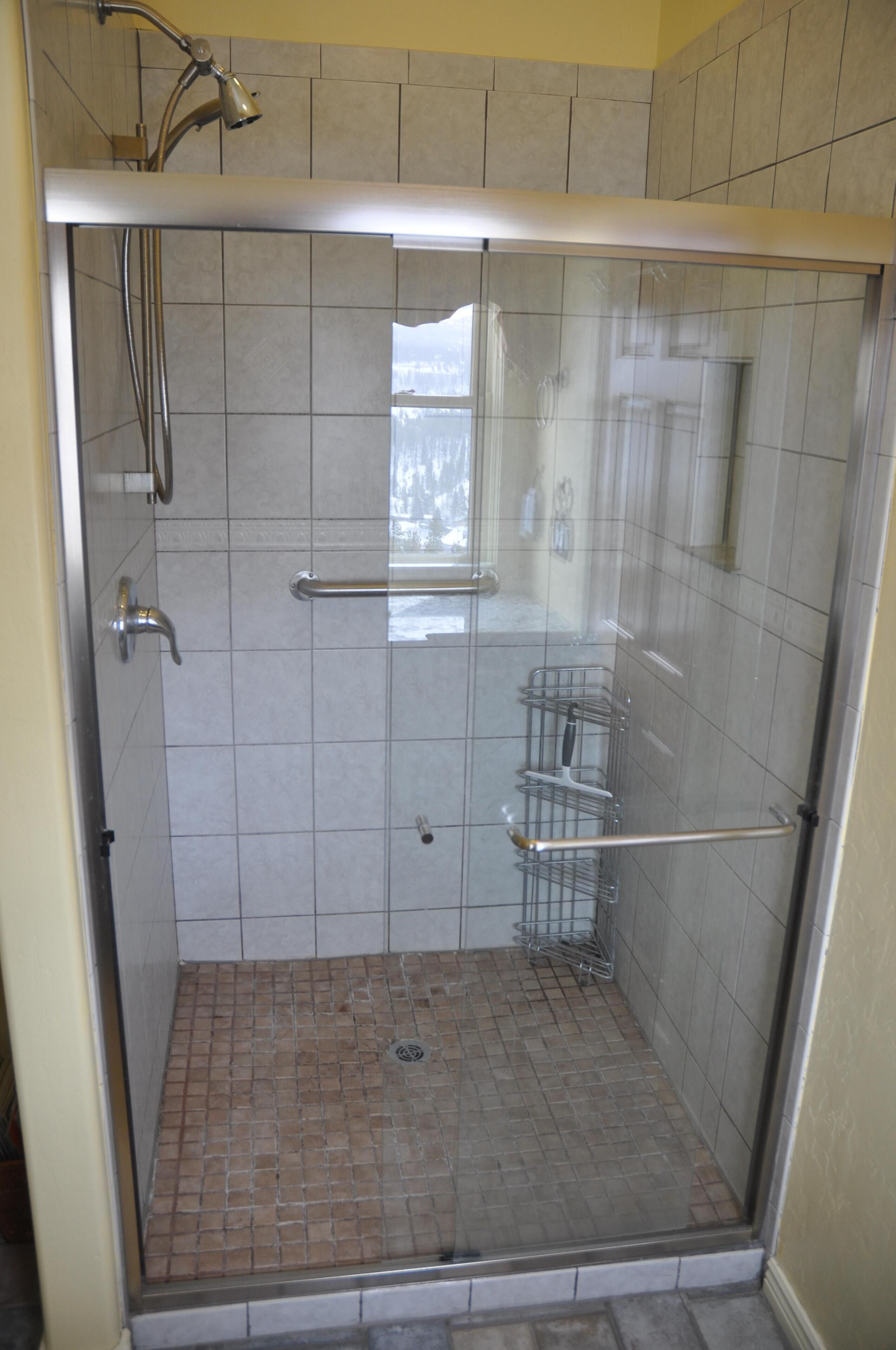 A glass-enclosed shower with a metal handle and a showerhead.